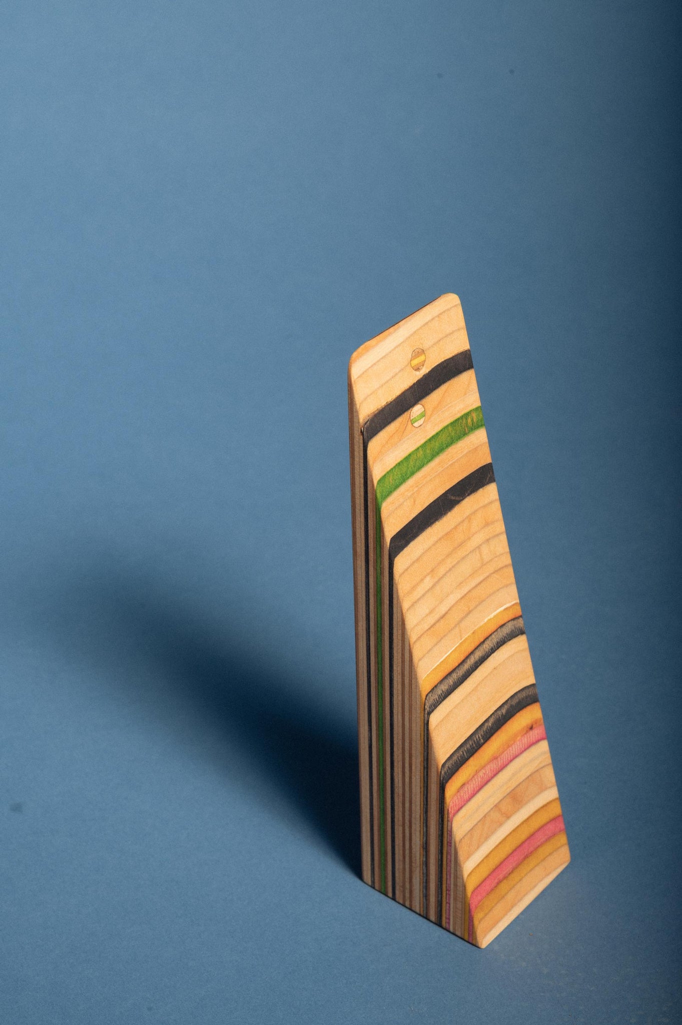 Door stop standing up on it's back face, showing the multicolored layers of recycled skateboard wood