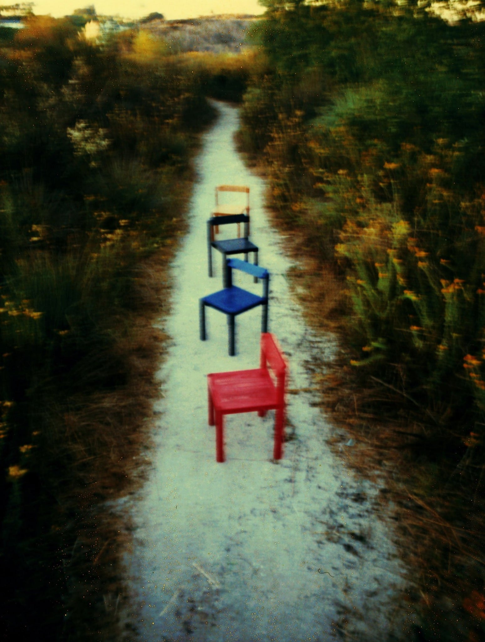 Red, Blue, Black, and Natural finish Anything Chairs lined up along a dirt walking path.