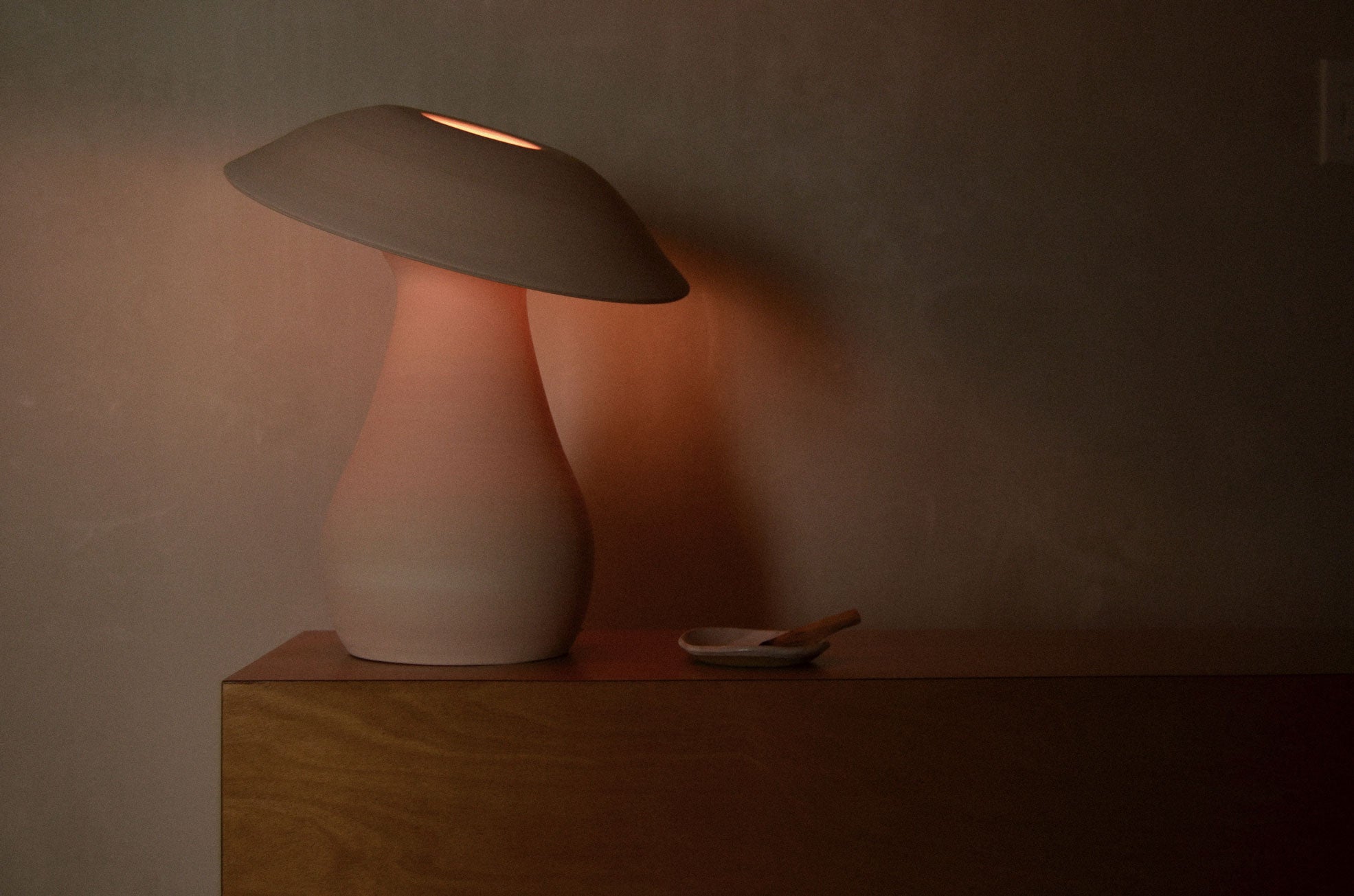 White Mushroom Lamp lit, set on a wood case piece