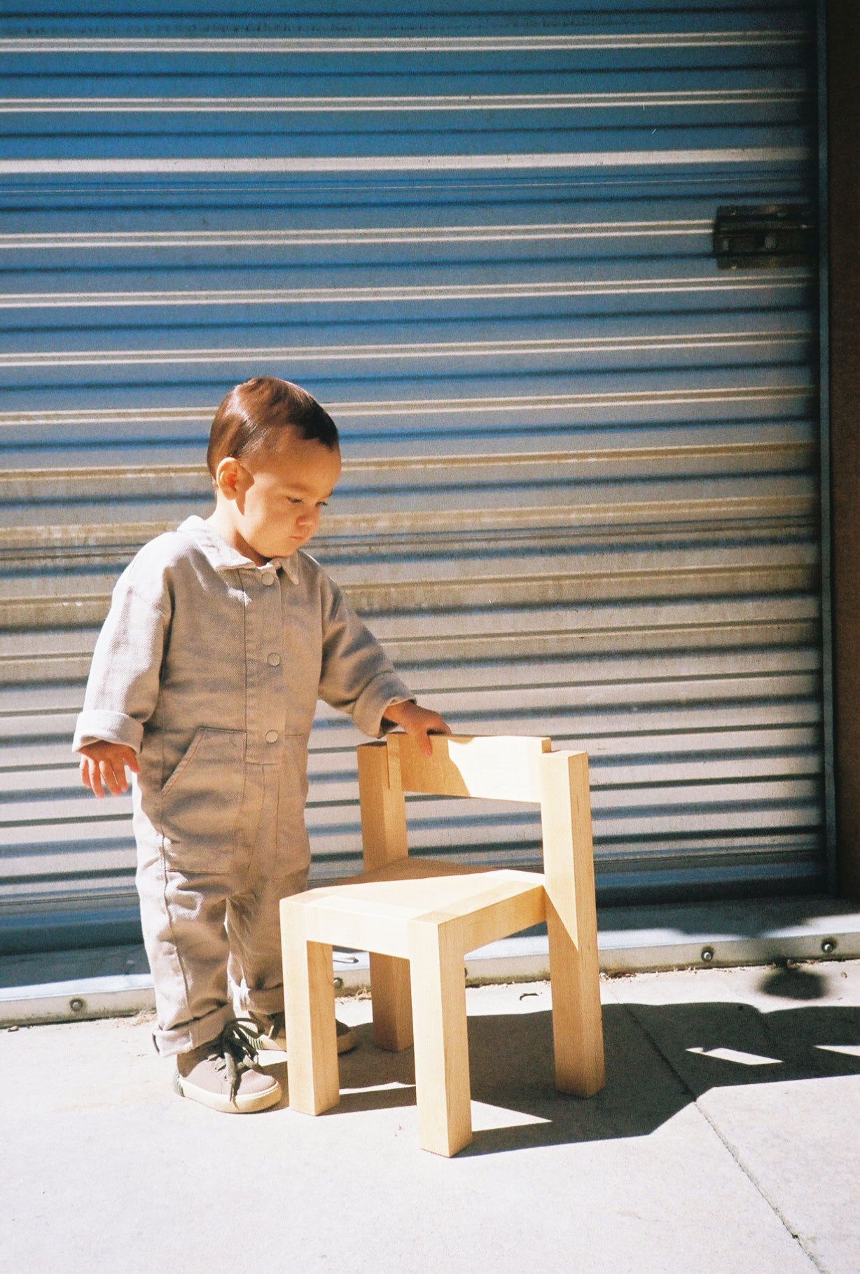 Child standing next to Natural finish the Child's Anything Chair shot outside