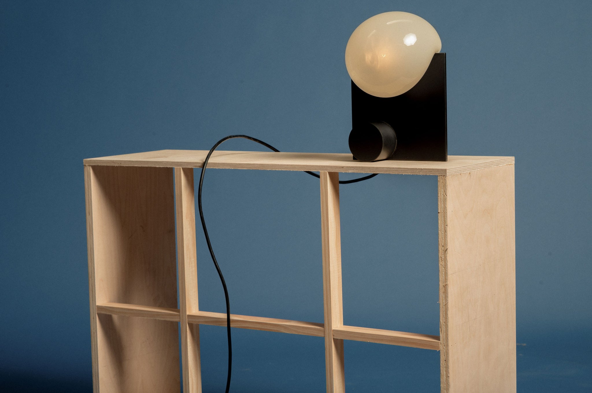 Bloop Table Lamp set on a ply-wood shelf on a blue backdrop