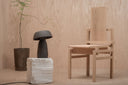 Tall Boy chair next to Mushroom lamp on a white pedestal shot in a plywood space