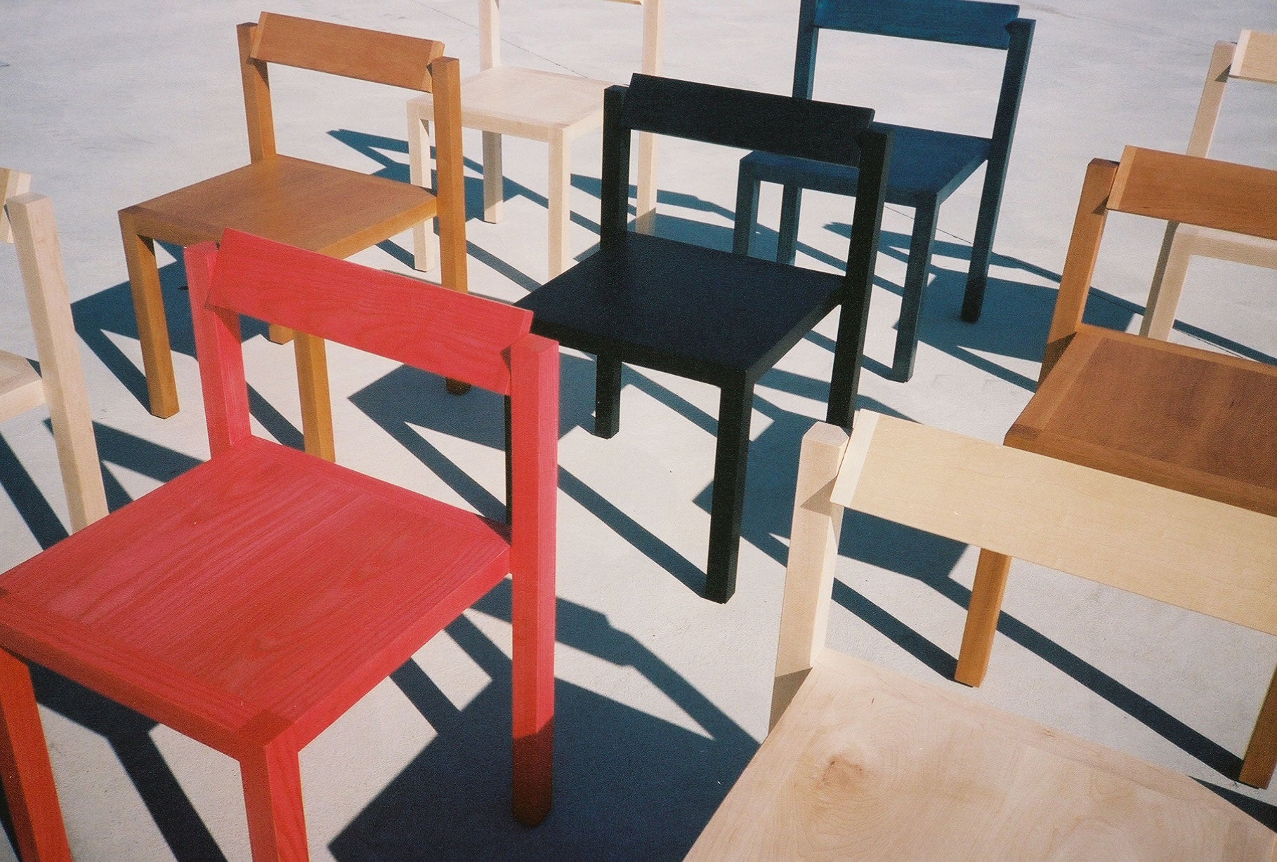 Red, Black, Blue, and an assortment of natural finish Anything Chairs arranged on concrete.