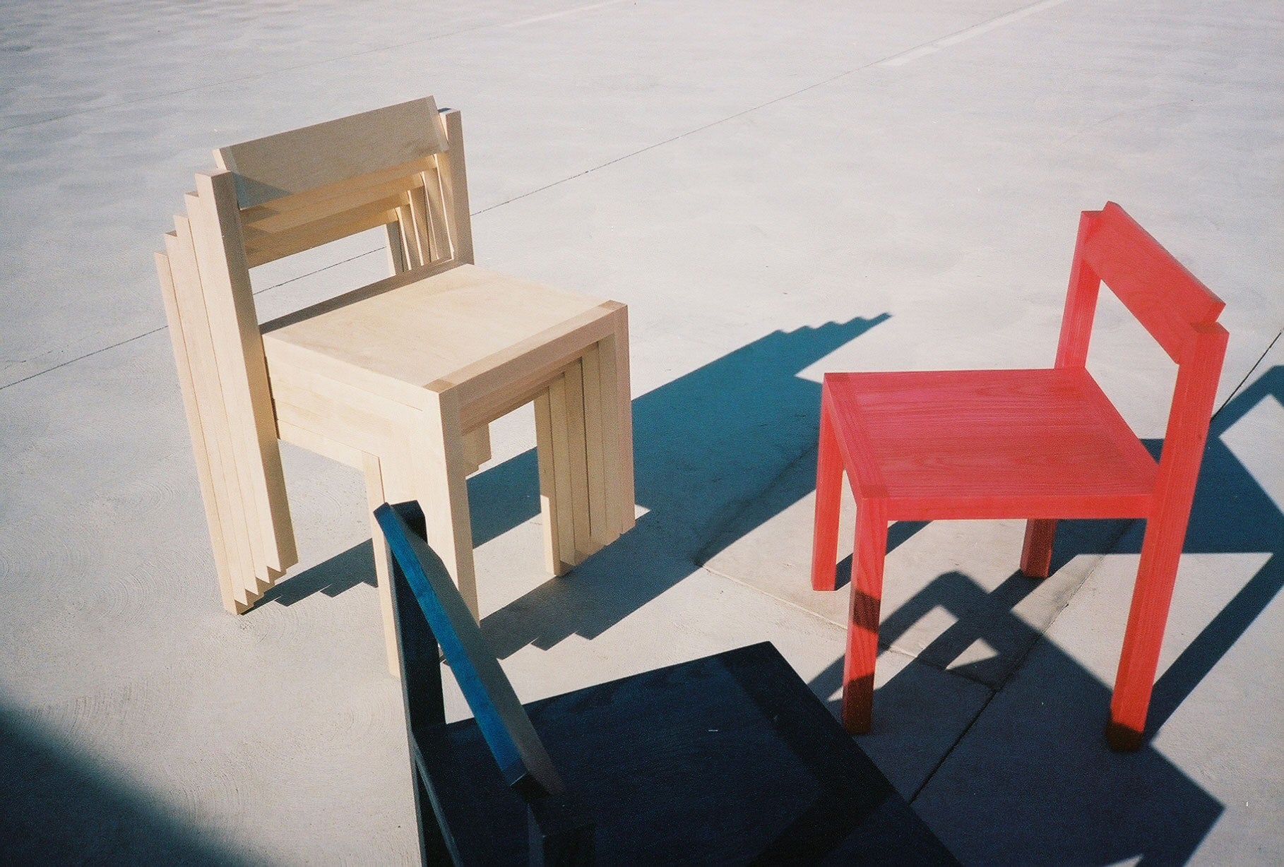 Red, Black, and an assortment of natural finish Anything Chairs stacked on concrete.