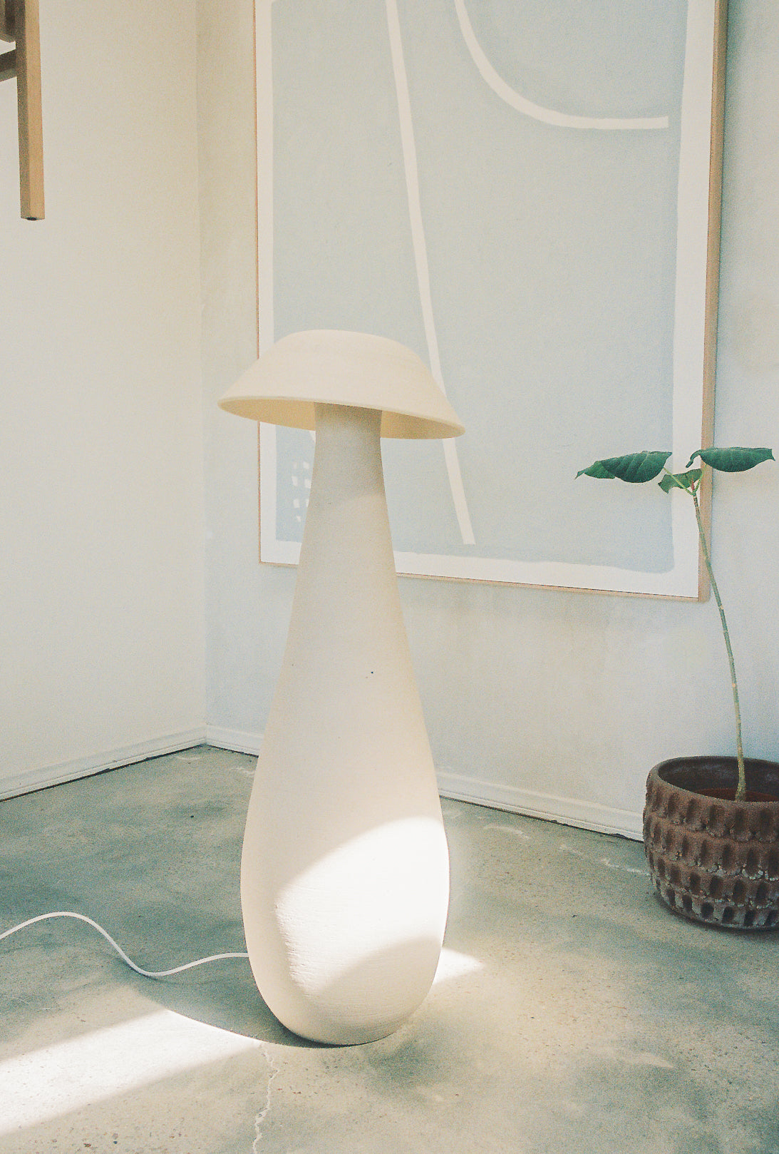 Mushroom Floor Lamp in white in the corner of a naturally lit room next to a potted plant.
